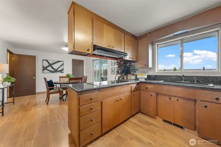 This kitchen features wood cabinetry, granite countertops, and a sizeable window above the sink with backyard views. The adjacent dining area and eating space create a functional layout for daily living and entertaining.