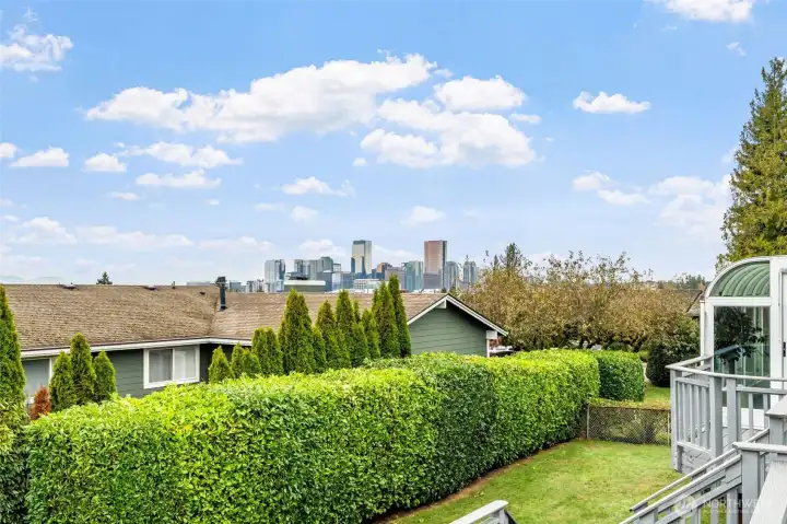 This elevated backyard view captures the Bellevue skyline beyond lush privacy hedges and neighboring rooftops. The deck offers a scenic vantage point for enjoying city views in a peaceful residential setting.