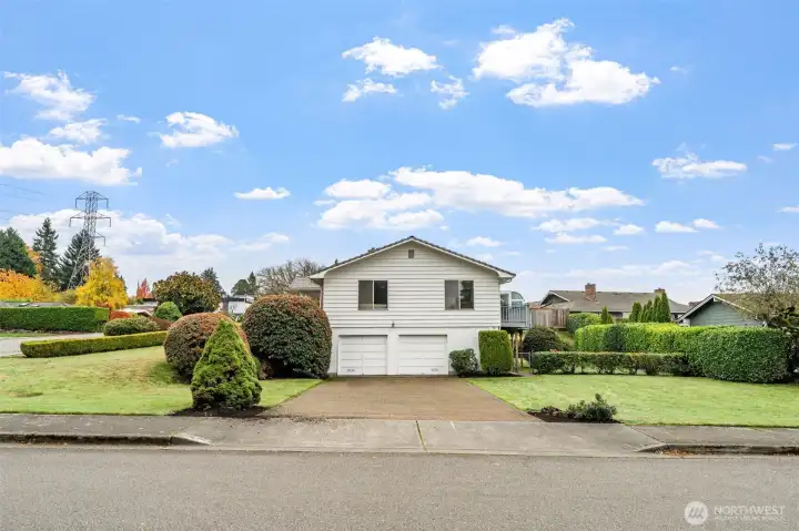 Side exterior view showcases a dual garage with a brick driveway and a fully landscaped yard. Mature shrubs and privacy hedges frame the space, offering a clean and well-maintained look.