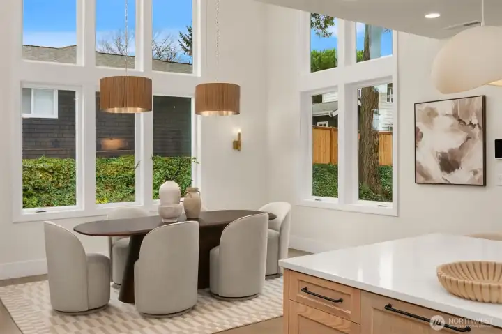 Light-filled dining area featuring soaring over 18 foot ceilings and open sightlines visible from the upper level.