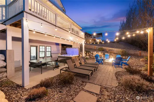 Twilight view of the home's outdoor entertaining area w/ landscaped yard, ping pong table & private hot tub.