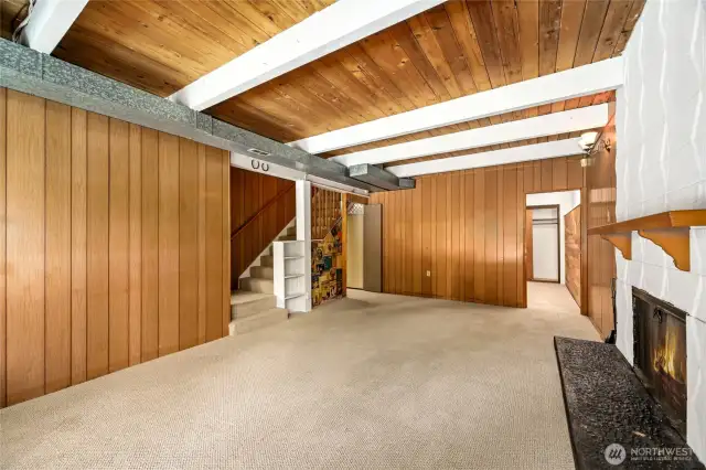 Downstairs family room looking back toward large bedroom or office space on right, stairwell to upstairs, and breezeway to laundry room in center of photo.