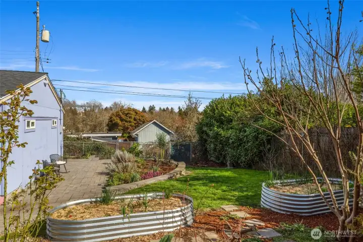 The large, finished outbuilding is to the left, alley behind the fence in back and a view of the 2nd, pavered patio area in backyard