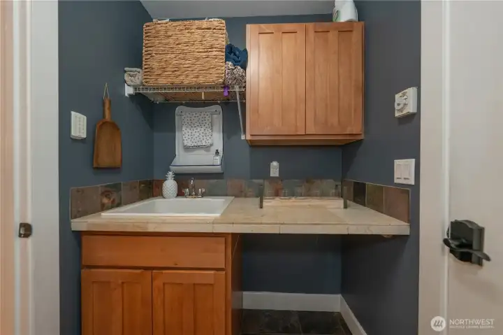 One side of the laundry room has a utility sink, counter top and storage cabinet.
