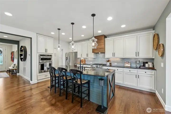 White cabinets combined with blue cabinets on the island, uppers with undermount lighting. Gas range with a decorative hood, a gorgeous tile backsplash and pendant lighting.