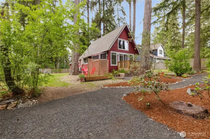 The bold red exterior, crisp white trim, and natural landscaping create an inviting, getaway-ready vibe, while the gravel path and rustic front porch add to its cozy, private feel.