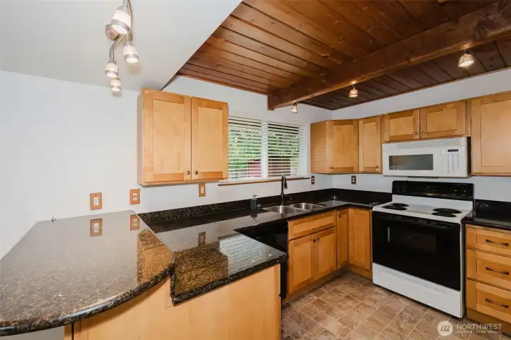 Natural wood cabinetry, granite-style counters, and a beautifully accented ceiling create a warm, high-impact look, while the lighting and layout make everyday living easy. The window over the sink fills the space with soft natural light and peaceful forest views, giving the kitchen that unmistakable “this is home” feeling you will love.