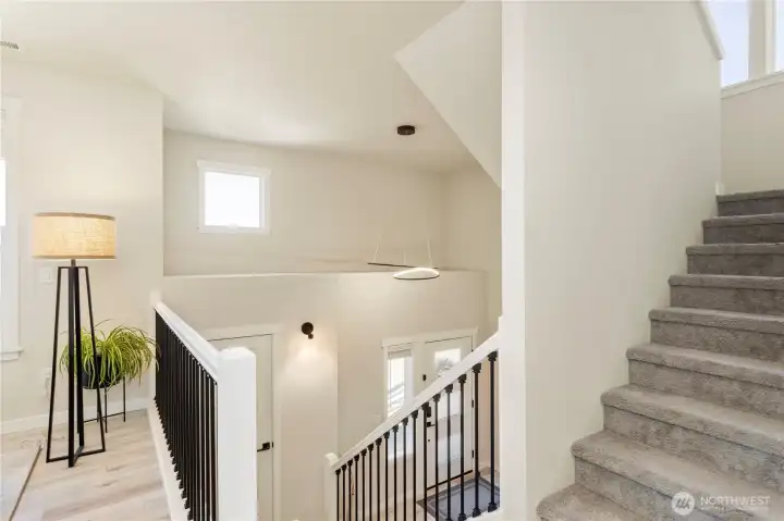 Light-filled split-level staircase showcases modern black iron balusters, a contemporary geometric chandelier, crisp white trim, and premium low-pile carpeted stairs. Light-filled split-level staircase showcases modern black iron balusters, a contemporary geometric chandelier, crisp white trim, and premium low-pile carpeted stairs.