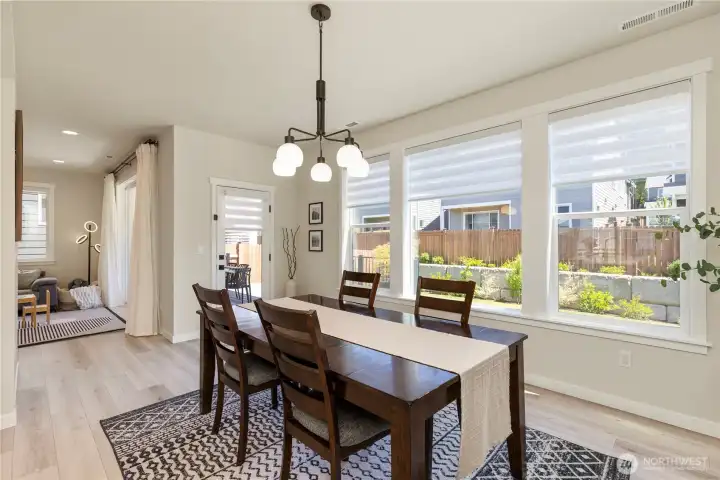 Light and bright dining area seamlessly adjacent to the kitchen, featuring wide-plank flooring, modern designer lighting, and large windows with custom motorized blinds Light and bright dining area seamlessly adjacent to the kitchen, featuring wide-plank flooring, modern designer lighting, and large windows with custom motorized blinds