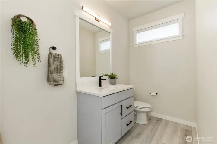 Main level powder room features a modern vanity with slab countertops, premium fixtures, updated contemporary lighting, and low-maintenance wide-plank flooring. Main level powder room features a modern vanity with slab countertops, premium fixtures, updated contemporary lighting, and low-maintenance wide-plank flooring.