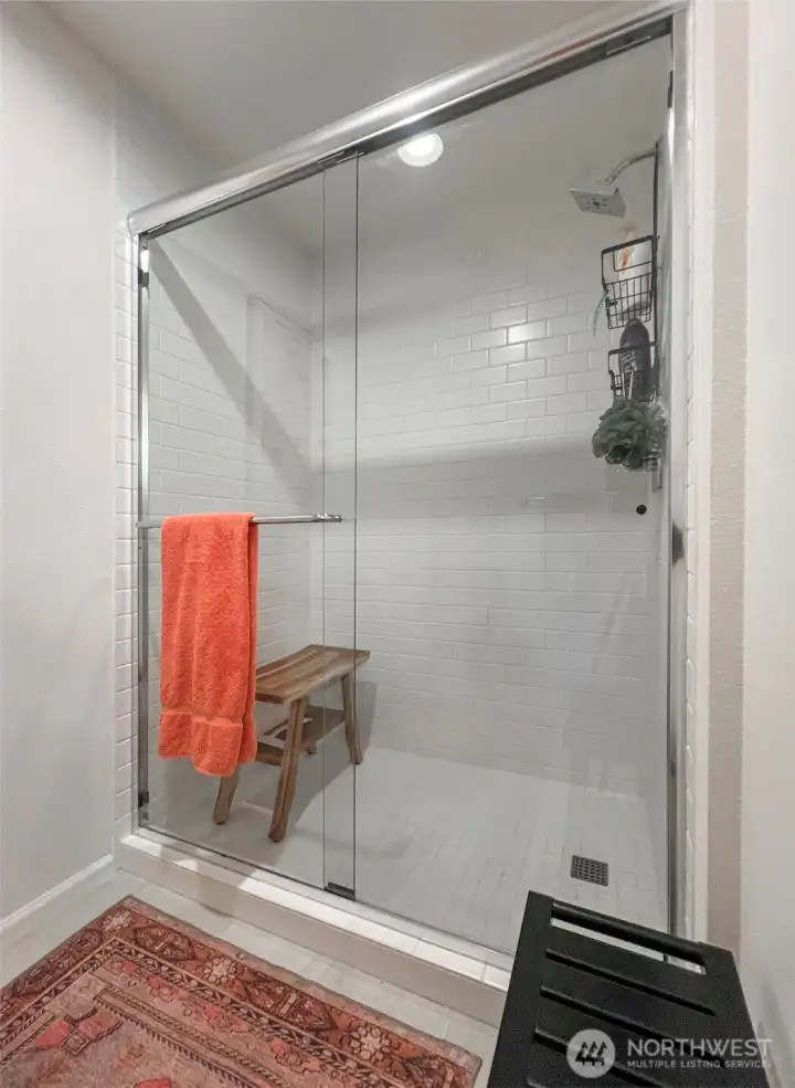 Oversized, tiled shower with glass doors and space for a seat.