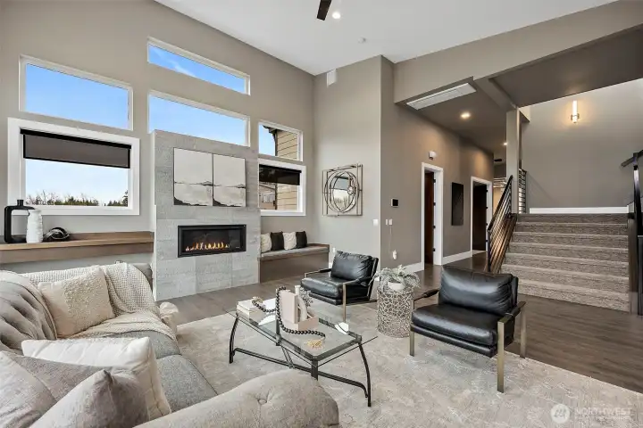 Bright, open living room in a modern home for sale in the River Rock community, featuring floor to ceiling windows, a contemporary fireplace, and abundant natural light. The spacious layout and scenic outdoor views create an inviting space ideal for relaxing or entertaining.