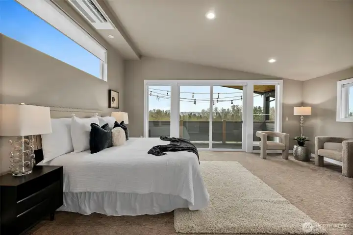 Spacious primary bedroom in this River Rock home in Auburn featuring large windows, soft carpeting, and abundant natural light. The open layout provides a comfortable retreat with plenty of space for a sitting area and relaxing views of the surrounding landscape.