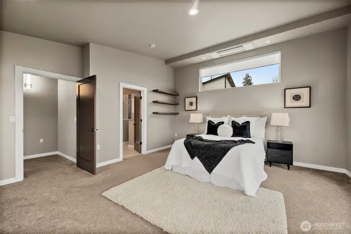 Spacious primary bedroom in this River Rock home in Auburn featuring large windows, soft carpeting, and abundant natural light. The open layout provides a comfortable retreat with plenty of space for a sitting area and relaxing views of the surrounding landscape.