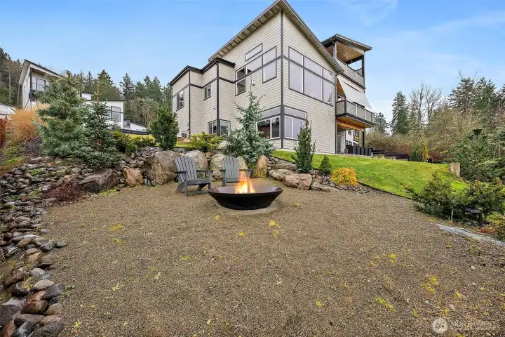 The backyard showcases a thoughtfully designed outdoor gathering area with a fire pit surrounded by terraced landscaping and natural stone accents. This private outdoor space supports relaxed evenings, entertaining, and enjoying the peaceful surroundings.