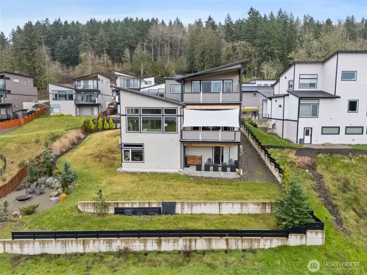 Modern exterior of a contemporary home for sale in the River Rock subdivision, featuring clean architectural lines, stone accents, a spacious driveway, and attached garage. Aerial and front views highlight its setting within the scenic River Rock community surrounded by natural greenery.