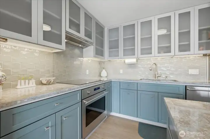 Cool seaside colors in soft marbled pattern make this counter top so gorgeous and the perfect backdrop for any meal, buffet or party. Dove gray glass tile backdrop flows around the kitchen  with under cabinets lighting. all this storage and space without blocking any of the amazing view.