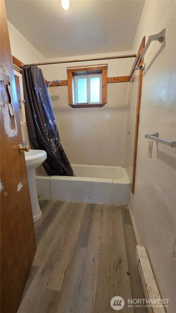 Full bathroom has new flooring, tub, pedestal sink and toilet
