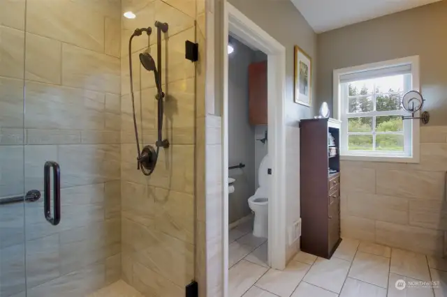 Beautifully tiled shower with grab bar and private water closet with storage.