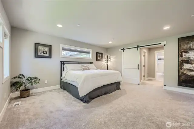 Relaxing primary suite with treetop views, barn door detail, his-and-hers walk-in closets and 5-piece spa bath.