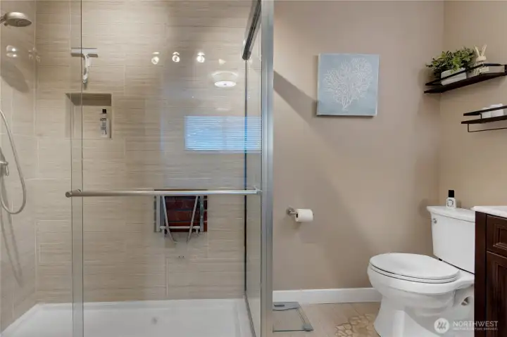 Spa inspired bath en suite, a large walk-in shower with built-in bench, newer toilet, vanity, custom tile flooring and shelving is all you need for your morning routine!