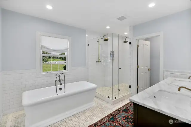Primary bathroom on the main level with marble floors and countertops, frameless shower doors, unlacquered brass fixtures from Newport Brass, dual showerheads, subway tile and freestanding bathtub.