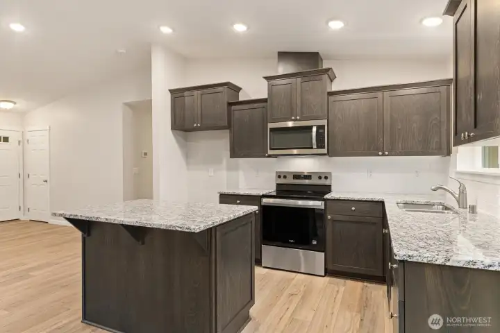 Stylish kitchen with stone countertops, stainless appliances, dark cabinetry with soft-close drawers + full height tile backsplash.