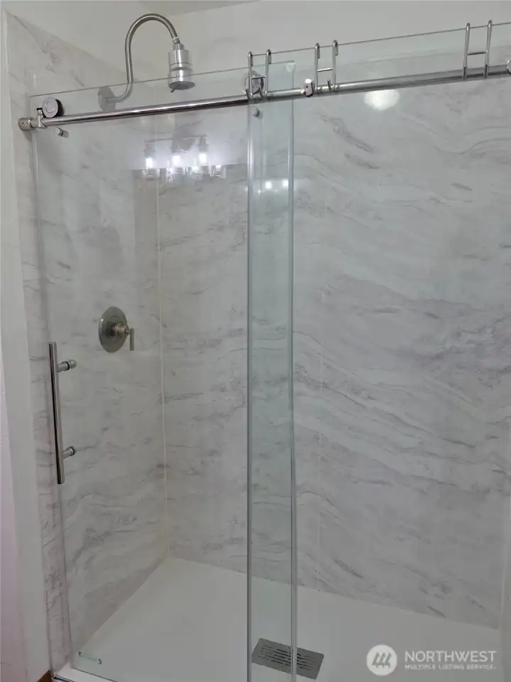 Bathroom w/ a full walk-in shower and marble walls.
