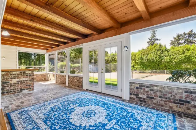 With its rustic brick and walls of glass, and integrated bar with a cutout to the kitchen, this sunroom combines natural elements with modern convenience to create a harmonious space that invites you to relax, entertain, and walk out to the beautiful stone patio and sport court. A small, gas-fired freestanding fireplace keeps the room toasty.