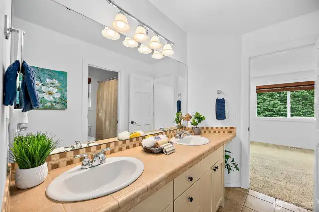 The en-suite/Jack and Jill bathroom for bedrooms 3 and 4 has dual vanities, tile counters and tile flooring.