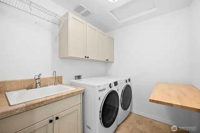 Upper level laundry room with cabinets, a folding table, a utility sink with tile counters and tile flooring.