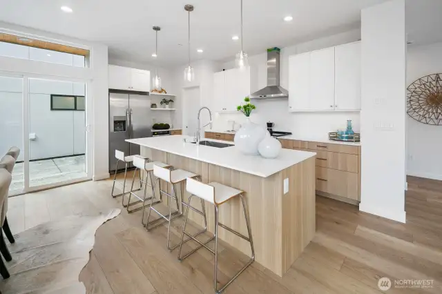 Chef’s island kitchen with counter, stainless appliances, and warm wood accents anchors the heart of the home. Photos are of model home 8825, finishes and floorplan may vary.