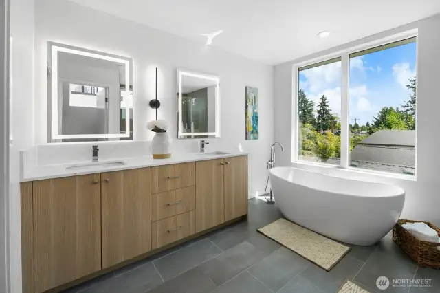 Luxe primary bath retreat: dual floating vanities, sculptural soaking tub, and treetop views. Photos are of model home 8825, finishes and floorplan may vary.