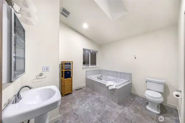 Spa-like en suite bath features soaking tub, vaulted ceiling, and peaceful views.