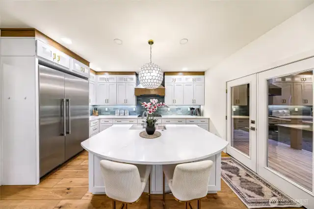 Kitchen reveals seamless flow between prep, dining, and outdoor access with island sink and custom hood.