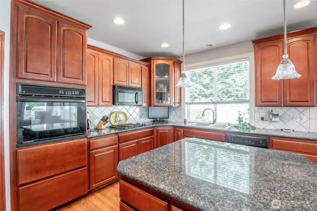 Large kitchen with island and granite countertops and full height tile backsplash and custom built cabinets.