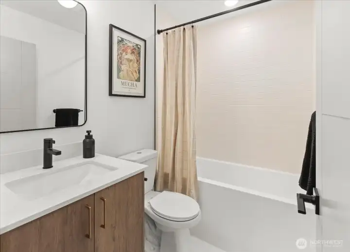 A clean, modern bathroom showcases soft-toned tilework, matte black fixtures, and a wood vanity with quartz counter.
