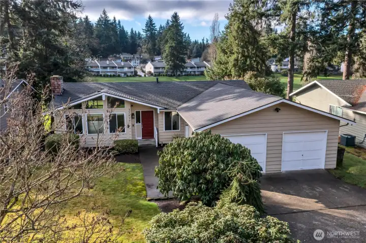Street-facing view with wide driveway, mature landscaping, and attached two-car garage.