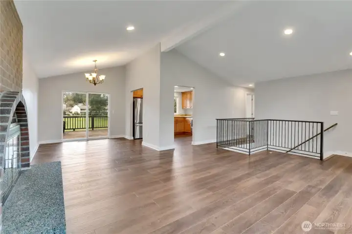 Open living and dining area with vaulted ceilings, updated flooring, and access to rear deck.