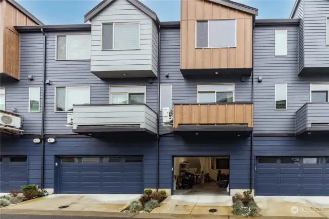 The back of the townhome with the garage entrance, balcony/deck, and a modest gardening area