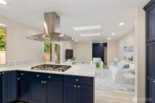 Kitchen gas cooktop, quartz counter tops, stainless hood. Virtually staged family room in the background