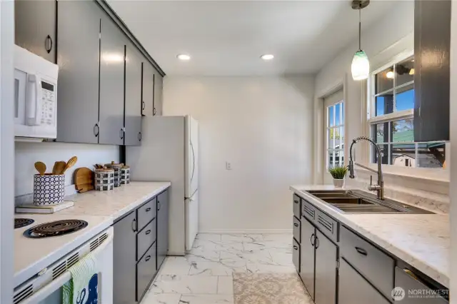 The updated kitchen is finished with new countertops, new flooring, freshly painted cabinets, and good lighting. The back door leads to the new patio just a few steps below.