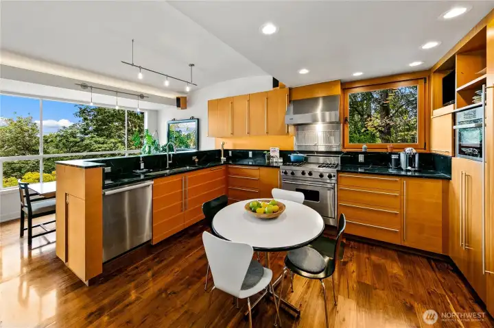 A circular breakfast table gathers light from walls of glass, making every meal feel like dining in the park. Walnut cabinetry and high-end appliances complete a kitchen where daily life flows with ease and connection to nature.