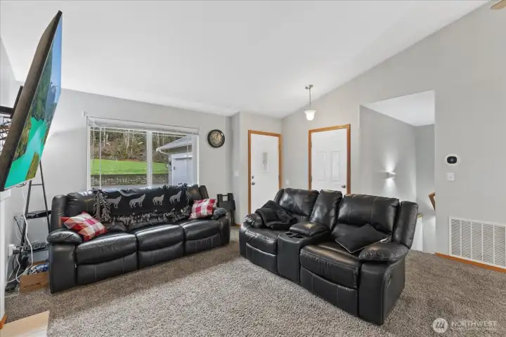 Living room view. Home entrance and garage doors in background. Stairway leads to lower level