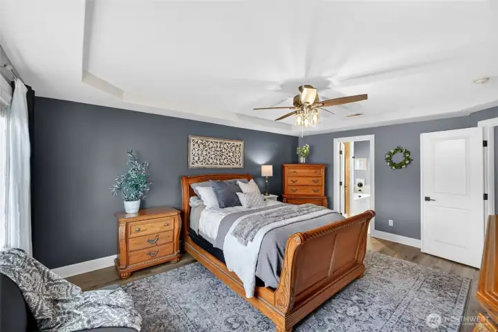 Primary features LVP flooring, tray ceiling, and ceiling fan.