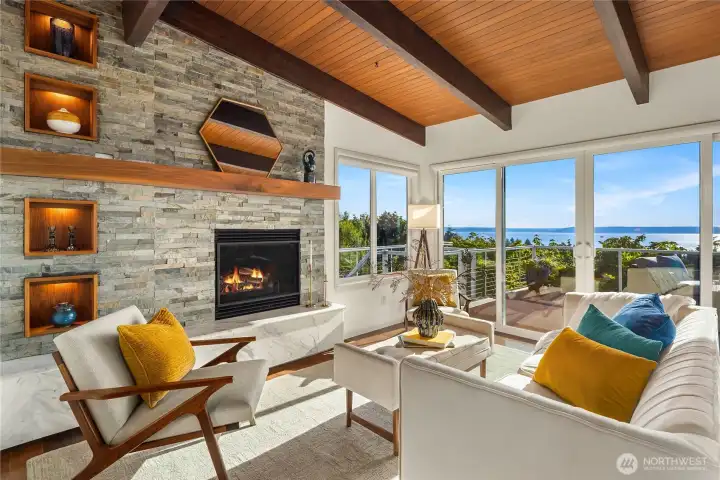 New fireplace added in 2021 with a marble hearth and stone surround. LED accent lighting in display boxes. First set of sliding glass doors that open to a large deck. Steps to the left lead down to the lower patio, workshop, utility room, and storage room.