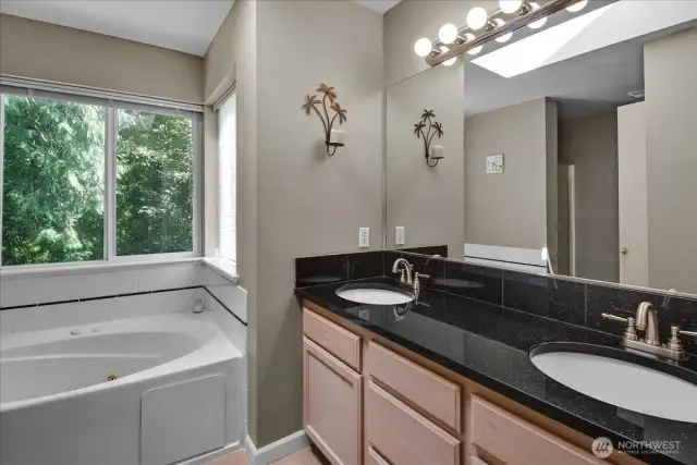 Primary bathroom features maple cabinets, slab granite countertops, dual sinks, soaking tub & shower. Window overlooks private backyard. Overhead skylight provides soft natural light.