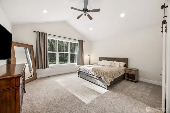 Primary Bedroom Suite with vaulted ceiling view to the private backyard that's surrounded by evergreen trees. Sliding barn-style door to right leads to ensuite.