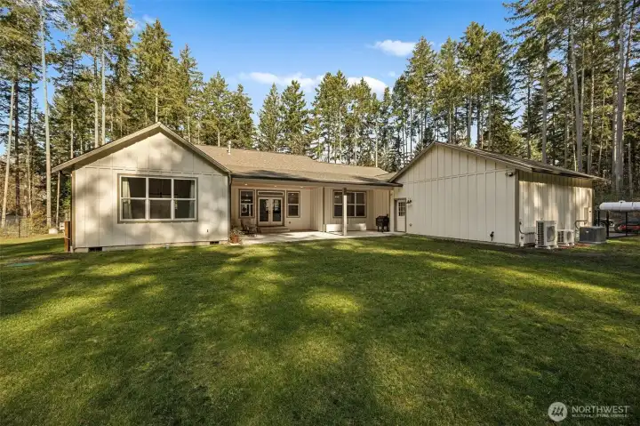 Back of home is very private, fully-fenced and surrounded by towering evergreen trees providing abundant privacy. Window on left side of home is primary suite, center is the covered patio & French doors to family room, window to right is the dining nook, garage is to the right. Also note: next to the heat pumps is an installed generator.