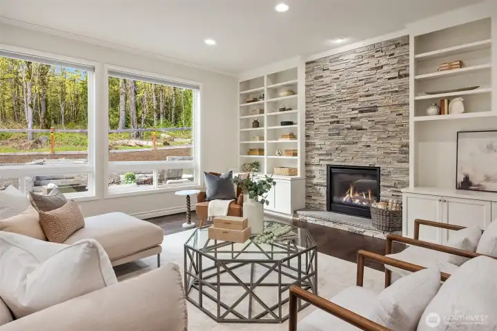 Refined and inviting, this elegant family room is anchored by a striking floor-to-ceiling stone gas fireplace and complemented by bespoke built-in cabinetry. Expansive windows frame serene natural surroundings, while wide-plank hardwood floors add warmth and timeless sophistication.